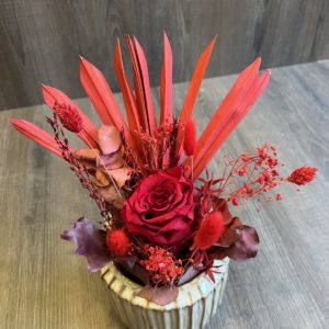 Arrangement avec une rose éternelle rouge et fleurs séchées dans les tons de rouge/bordeaux