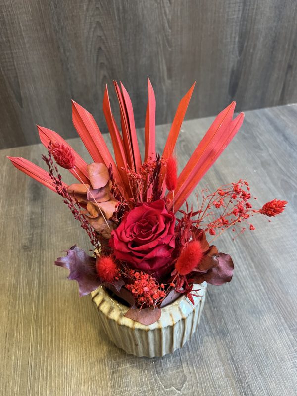 Arrangement avec une rose éternelle rouge et fleurs séchées dans les tons de rouge/bordeaux